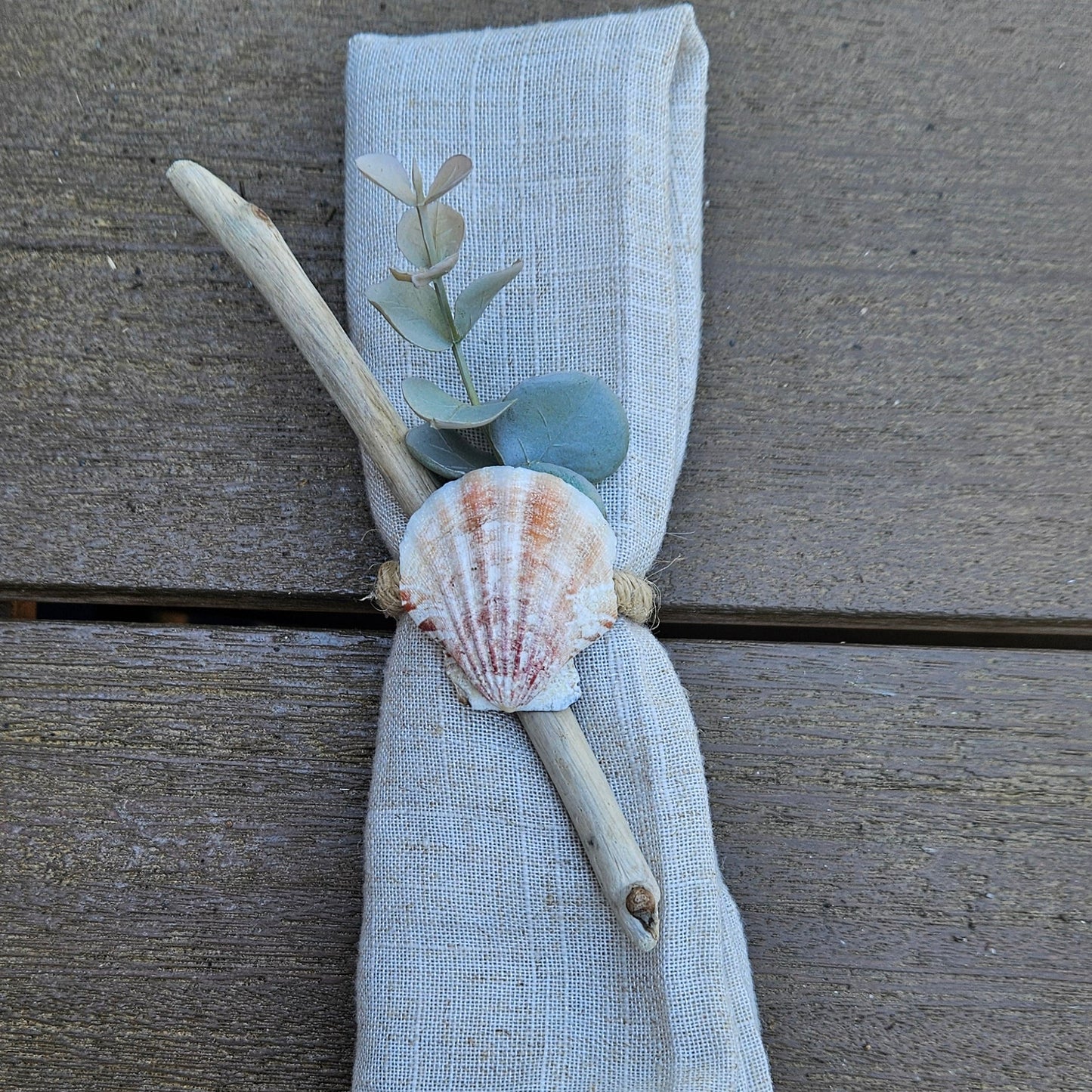 Folded light blue napkin with a shell and branch on a wooden surface