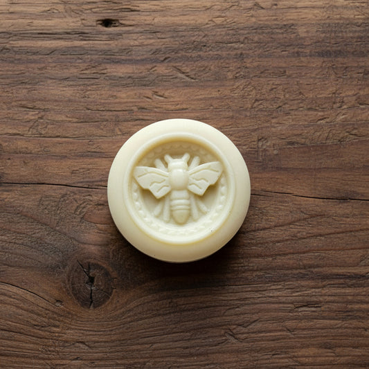 Round lotion bar with a bee design on a light wooden surface