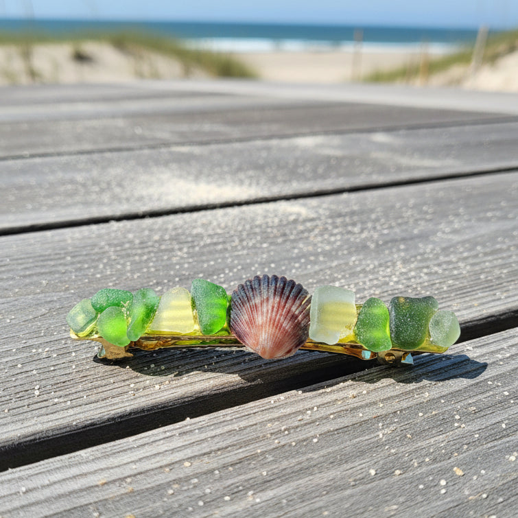 A handmade barrette made of green glass beads and a small brown shell, laid flat on a brown wooden surface.