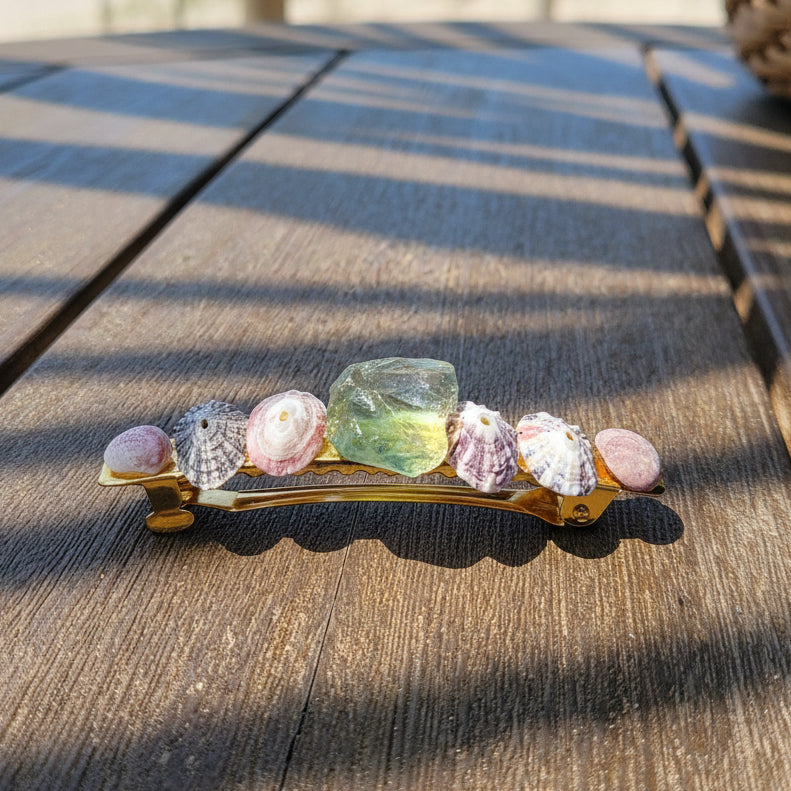 A handmade barrette made of pink, clear, and green stones, lying on a brown wooden surface.