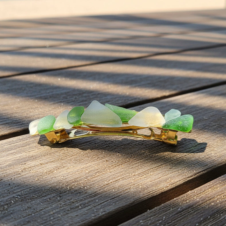 A small hair claw clip with green and white shell pieces and gold-tone metal, shown on a brown wooden surface.
