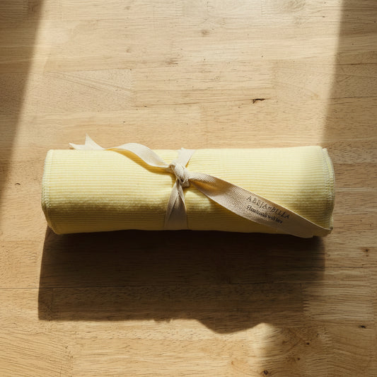 Rolled-up yellow  reusable towel with a white ribbon on a wooden surface next to books.