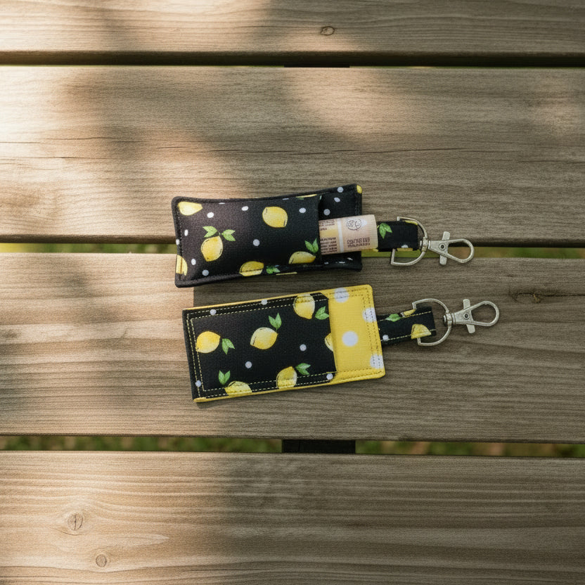 Two keychain lip balm pouches with lemon pattern on a wooden surface