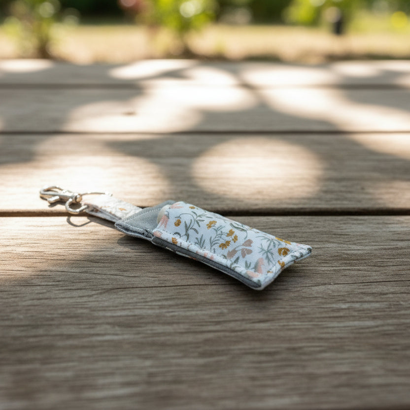 Fabric lip balm holder keychain with floral pattern on a wooden surface