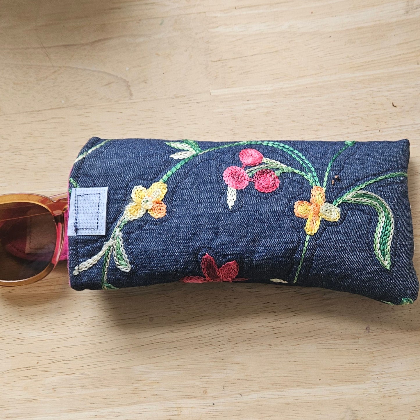 Floral embroidered sunglasses case on a wooden surface