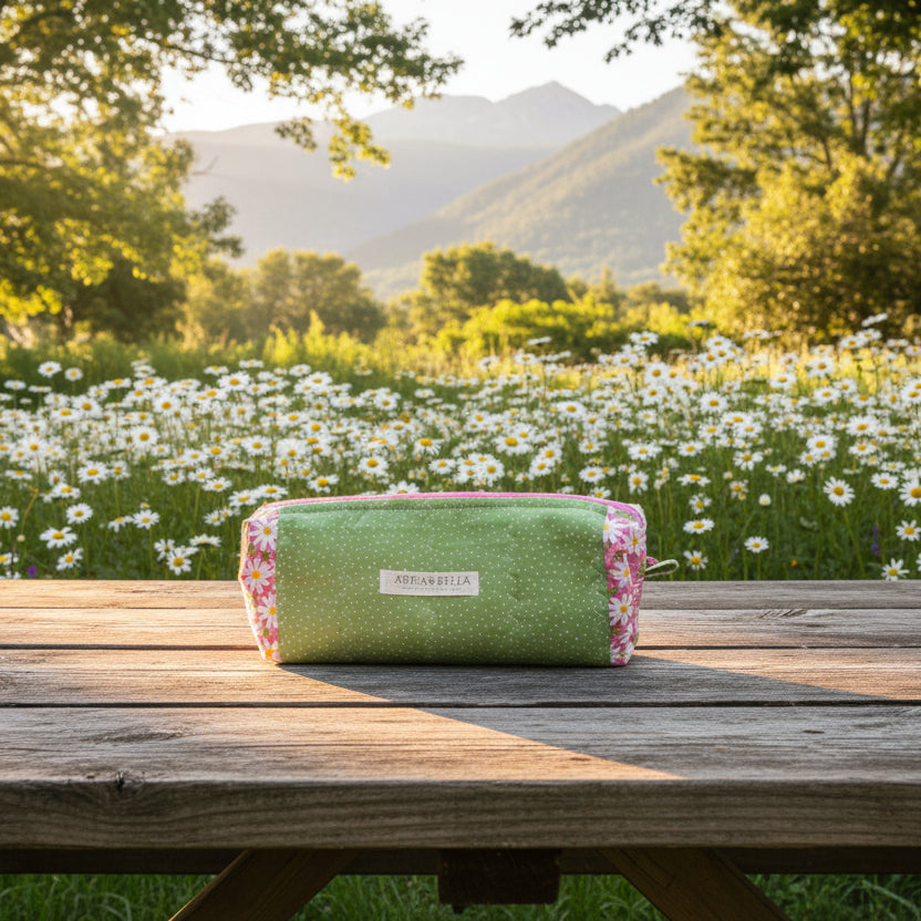 Green and pink cosmetic bag with floral pattern on picnic bench overlooking daisy field