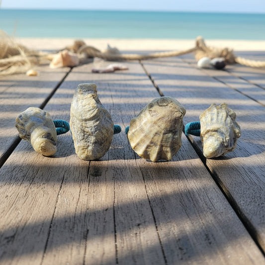 A handmade napkin rings made of  small, irregularly shaped sea shells in natural beige and white tones, strung on a turquoise blue cord, resting on a weathered wooden table.