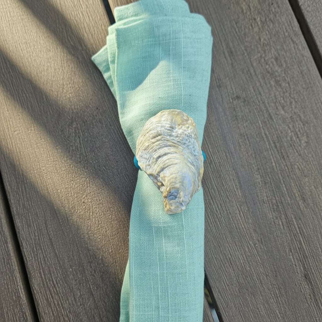 A folded white linen napkin on a dark brown wooden table, secured with a decorative shell ring featuring small turquoise blue accents.