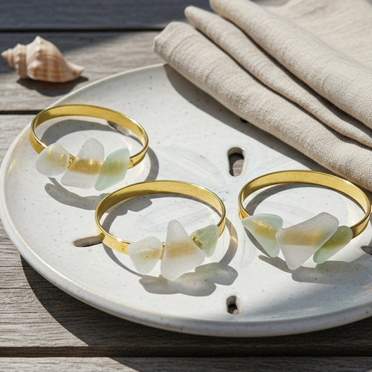 A gold-toned metal napkin ring with several irregular white sea glass accents, photographed against a brown wooden surface.