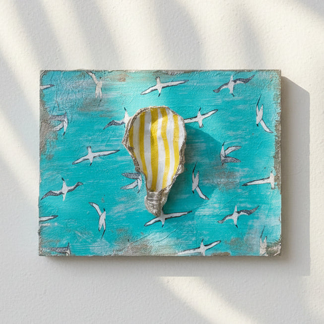 A square turquoise decorative plaque featuring a central striped shell motif surrounded by small white seagull silhouettes, placed on a light wood tabletop.